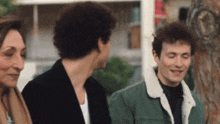 a man in a green jacket with a sherpa collar talks to two other men
