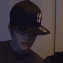 a man wearing a ny hat and glasses is smiling in the dark .