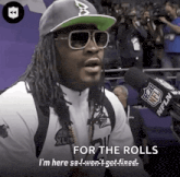 a man wearing sunglasses and a hat says " for the rolls " in front of a microphone