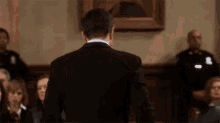 a man in a suit stands in front of a group of people in a courtroom