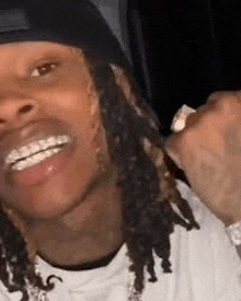 a man with dreadlocks is smiling and wearing a hat .