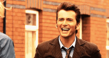 a man in a suit and tie is laughing in front of a brick wall .