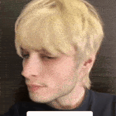 a man with blonde hair and a beard is wearing a black shirt and looking at the camera .