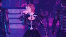 a woman is singing into a microphone on a stage in front of a crowd .