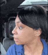 a woman wearing a blue jacket and a necklace is sitting in the back seat of a car
