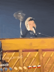 a man is singing into a microphone while sitting at a piano that says aiscb