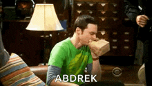 sheldon cooper from the big bang theory is sitting on a couch eating a bag of food .