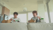 two men are sitting on a couch with boxes of food and a bottle of ketchup on the table