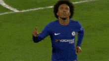 a soccer player wearing a blue yokohama jersey points upwards