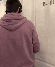 a man in a pink hoodie is standing in front of a door with the number b-61 on it