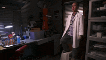 a man in a lab coat is standing on a stool in a dark room
