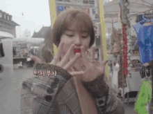 a woman in a plaid jacket is eating a red strawberry in a market .