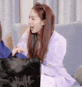 a woman in a purple shirt is sitting on a couch with her mouth open