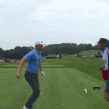 a man in a blue shirt and white hat is walking on a golf course