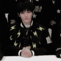 a young man wearing a black jacket with lightning bolts on it is sitting at a table .