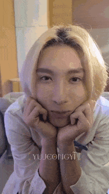 a young man with blonde hair is sitting on a couch with his hands on his chin .