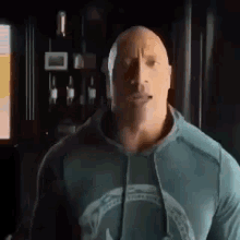 the rock is wearing a hoodie and looking at the camera in a dark room .