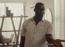 a man in a striped shirt stands in front of a shelf