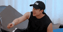 a young man wearing a black hat and a black tank top is sitting on a bed .