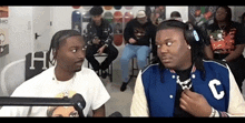 a man in a blue jacket with the letter c on it talks to another man