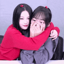 a girl in a red sweater is hugging another girl in a grey sweatshirt
