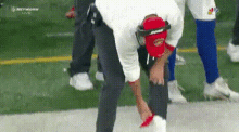 a man wearing a red hat and a white shirt is bending over on a football field .