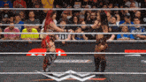 two women shake hands in a wrestling ring with a crowd in the stands