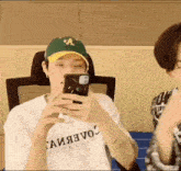 a man wearing a green hat is taking a picture of himself on his phone .