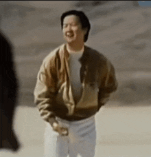 a man in a brown jacket and white pants is standing in a desert .
