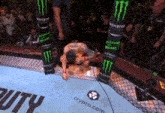 a man is kneeling down in a boxing ring with monster energy advertisements on the walls .