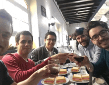 a group of men are sitting at a table toasting with wine glasses