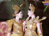 two women in gold costumes are standing next to each other in front of a sign that says ' grand celeb festival '
