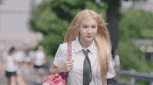 a girl with blonde hair wearing a white shirt and tie carrying a pink bag that says i love you