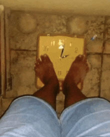 a person 's feet are standing on a scale with a clock on the wall behind them