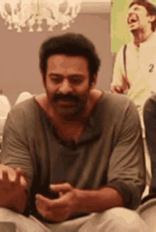 a man with a mustache is sitting in a chair looking at his phone .
