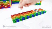 a person 's finger is pointing at a rainbow colored block that says made in animatica