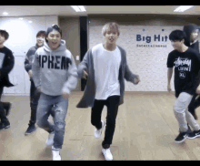 a group of young men are dancing in a room with a big hit entertainment sign in the background .