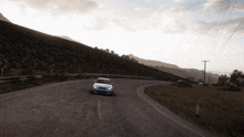 a white car is driving down a road with a hill in the background