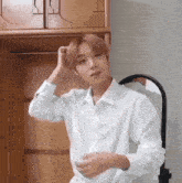 a young man in a white shirt is standing in front of a mirror and adjusting his hair .
