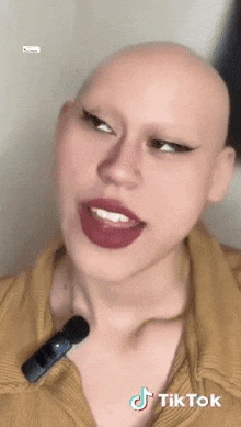 a woman with a shaved head and no eyebrows is talking into a microphone .