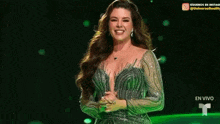 a woman in a green dress is standing on a stage with her hands folded and smiling .