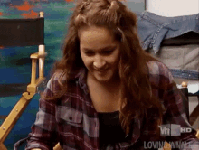 a woman in a plaid shirt is sitting in a director 's chair and smiling .