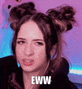 a woman with two buns in her hair is making a funny face and the word eww is on the bottom of her face .