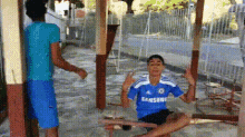 a boy wearing a blue samsung jersey is sitting on a swing