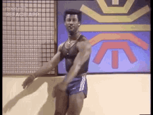 a muscular man is dancing in a gym in front of a wall with a logo on it .