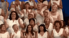 a large group of women are singing in a choir and clapping their hands .