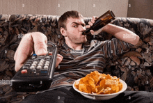 a man sits on a couch drinking beer and eating chips while holding a remote control