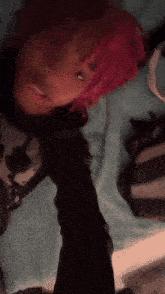 a person with pink hair is laying on a bed and taking a selfie .