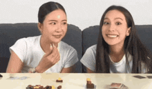 two women are sitting at a table playing a game and one of them is eating something .