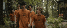 a group of people wearing orange shirts with a horse on them are walking through a forest